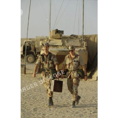 Soldats américains passant devant un VAB. L'un d'eux porte une mallette.