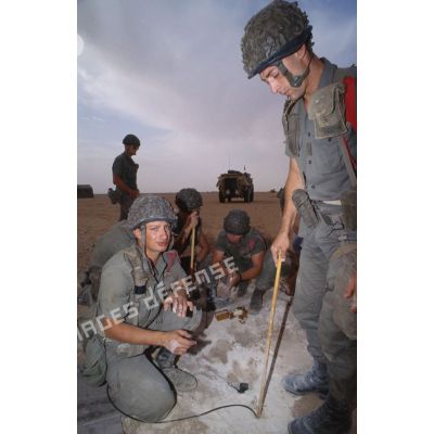 Des soldats du génie enfouissent des pains de plastic dans le sable et mettent en place des cordons détonants lors d'un entraînement au tir à l'explosif.