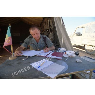 Un lieutenant de la Légion écrit les ordres du jour, assis à son bureau devant sa tente.