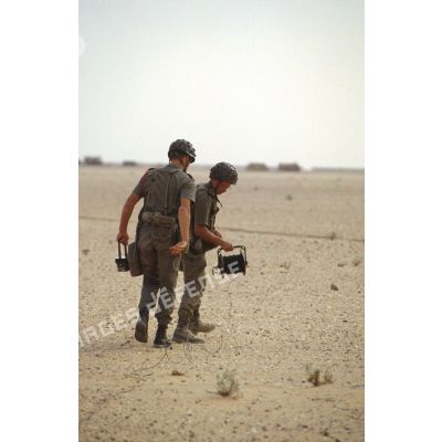 Deux soldats du génie mettent en place un dispositif de mise à feu élémentaire électrique dans le désert.