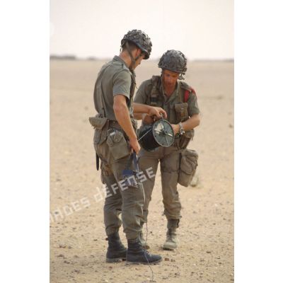 Deux soldats du génie mettent en place un dispositif de mise à feu élémentaire électrique dans le désert. L'un d'eux tient dans sa main droite l'exploseur.