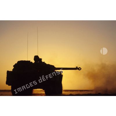 Tir d'un blindé de reconnaissance AMX-10 RC sur le pas de tir en contre-jour au coucher du soleil.