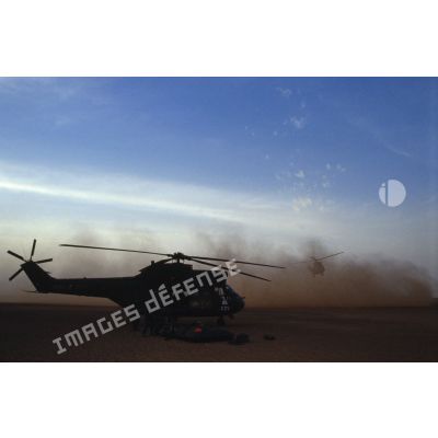Ravitaillement en carburant au sol d'un hélicoptère de transport Puma SA-330 après héliportage, tandis qu'un autre Puma atterrit.