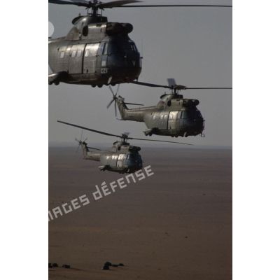 Trois hélicoptères de transport Puma SA-330 des 1er et 5e RHC survolent le désert en formation groupée lors de l'héliportage de groupes de combat du 1er RI vers la zone d'opération nord.
