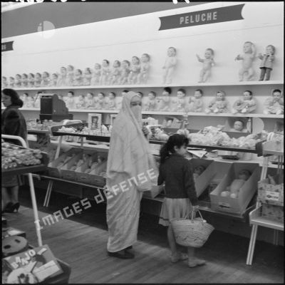 Une femme voilée et une enfant devant le rayon poupées d'un supermarché.