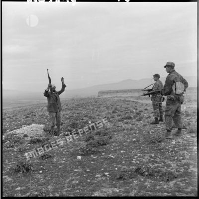 Un homme, mains en l’air et tenant un fusil, se rend devant deux soldats armés lors d’une opération héliportée sur le djebel Tarf.