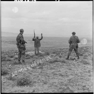 Un homme, mains en l’air et tenant un fusil, se rend devant deux soldats armés lors d’une opération héliportée sur le djebel Tarf.