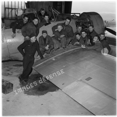 Mécaniciens et officiers de l'armée de l'Air autour d'un avion dans un hangar.