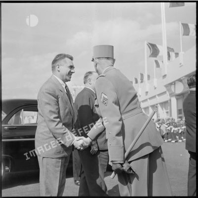 Un général serre la main à un homme devant l'entrée d'un stade lors d'une rencontre de football France-Belgique en Algérie.