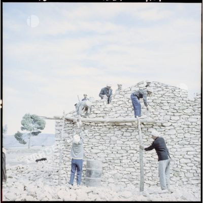 Un groupe d’hommes construit une maison en pierre dans la région d’Aïn Tindamine.