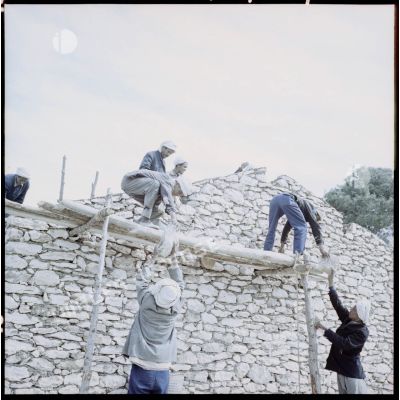 Un groupe d’hommes construit une maison en pierre dans la région d’Aïn Tindamine.