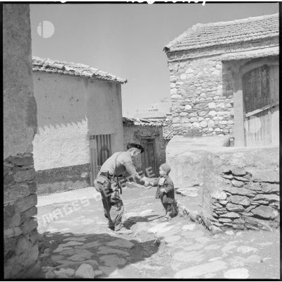 Un chasseur-alpin donne la main à un petit graçon dans la rue du village de Zaknoun.