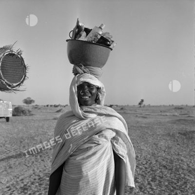 Portrait d'une femme tchadienne qui transporte divers objets dans une cuvette posée sur sa tête.