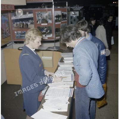 Une hôtesse renseigne des étudiants sur un espace du stand de l'exposition Jeunesse 1976, dans l'ancienne gare à Paris.