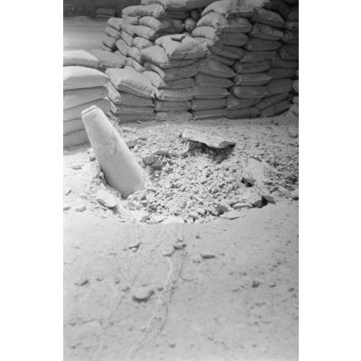Gros plan sur une bombe alliée qui n'a pas explosé en traversant le toit d'un hangar et en touchant le sol.