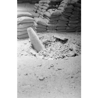 Gros plan sur une bombe alliée qui n'a pas explosé en traversant le toit d'un hangar et en touchant le sol.