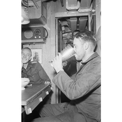 A la table réservée aux officiers du bord, un officier du sous-main U-boot U-203 boit un liquide contenu dans un Ehrenpokal.