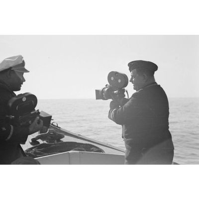 A bord d'un navire léger, non loin du port de Saint-Nazaire, deux cameramen et un photographe immortalisent le retour au port du sous-marin U-552 (non visible).