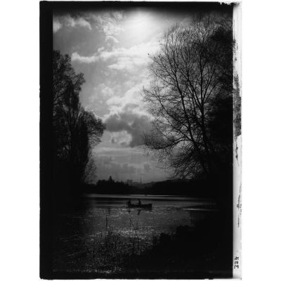 [Deux personnes naviguent sur un lac grâce à une barque, végétation en premier plan, vue en contre-jour.]