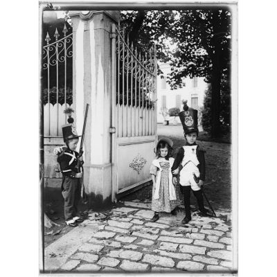 [Enfants habillés en adulte devant le portail d'une maison.]
