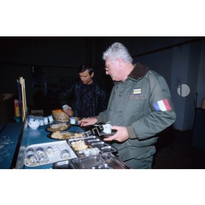 Le colonel Le Roux prépare son plateau repas près d'un civil blessé à la chaîne du réfectoire de l'aéroport de Sarajevo.
