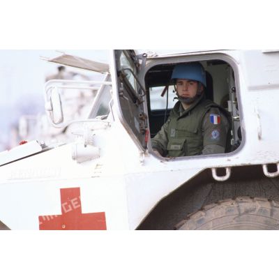 Portrait d'un conducteur de véhicule de l'avant blindé (VAB) sanitaire à son poste de pilotage, portière ouverte, arborant casque bleu et insigne de la 11e brigade parachutiste.