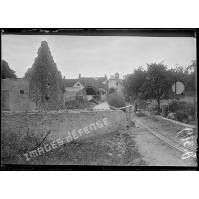 [Des soldats réparent une voie Decauville, qui passe à travers un village en ruine.]