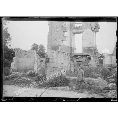 [Un soldat se tient debout devant une maison en ruine, à Vassogne.]