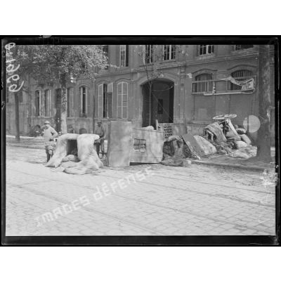 [Deux soldats devant une barricade composée de matelas, portes, chariots et table dans une rue de la ville de Reims.]