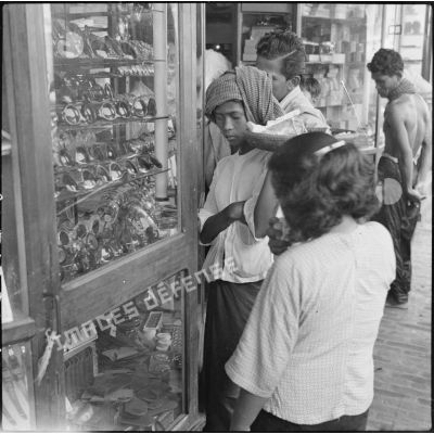 Cambodgiens et cambodgiennes regardant la vitrine d'une boutique chinoise qui vend notamment des lunettes de soleil.