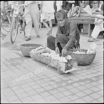 Une vendeuse de rue préparant des brochettes de bananes cuites au barbecue dans une rue.
