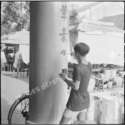 Un peintre décorateur en train de peindre des inscriptions sur une colonne dans une rue.