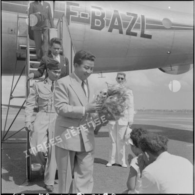 A sa descente d'avion, le roi du Cambodge Norodom Sihanouk reçoit un bouquet de fleurs.