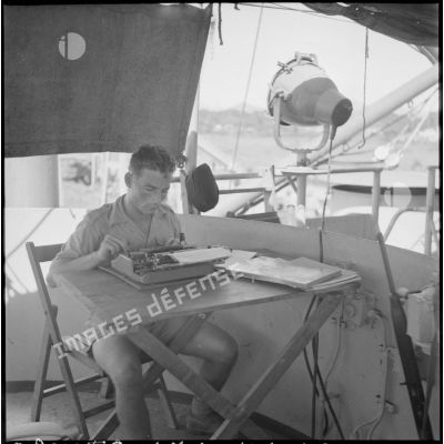 A bord du LST Rance, un caporal du GM 12 tape les ordres de son commandant sur une machine à écrire.