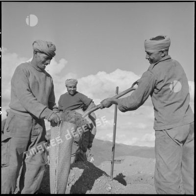 Des goumiers du 32e Goum du 5e Tabor remplissant de terre un sac de raphia qui servira à leur protection.