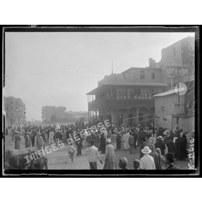 Port-Saïd, 7 h 20. La foule près d'un trou de bombe. A droite, le café près duquel la bombe est tombée (6 morts). [légende d'origine]