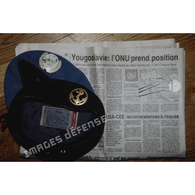 Béret bleu avec insigne ONU et béret Terre avec insigne Troupe de Marine mis en scène sur fond de journal évoquant l'intervention de la FORPRONU en ex-Yougoslavie.