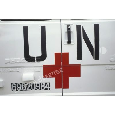 Gros plan sur la croix rouge et sigle "UN" (United Nations) sur fond blanc peints sur les portières arrière d'un véhicule de santé de la FORPRONU.