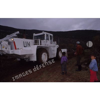 Aménagement  d'un terre-plein avec un moyen polyvalent du génie (MPG) du bataillon d'infanterie aux couleurs de l'ONU sous le regard d'un paysan et de ses enfants.