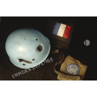 Vue d'au-dessus d'un casque bleu d'un sergent du 8e régiment d'infanterie (8e RI) ayant été blessé à la tête par balle en ex-Yougoslavie mis en scène sur une veste militaire avec le drapeau français et l'insigne de l'ONU.