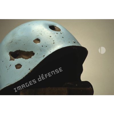 Impacts sur un casque bleu mis en scène sur fond blanc et appartenant à un sergent du 8e régiment d'infanterie (8e RI) ayant été blessé à la tête par balle en ex-Yougoslavie.