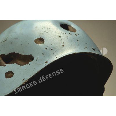 Impacts sur un casque bleu mis en scène sur fond blanc et appartenant à un sergent du 8e régiment d'infanterie (8e RI) ayant été blessé à la tête par balle en ex-Yougoslavie.