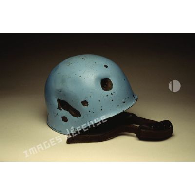 Casque bleu présentant des impacts mis en scène sur fond blanc et appartenant à un sergent du 8e régiment d'infanterie (8e RI) ayant été blessé à la tête par balle en ex-Yougoslavie.