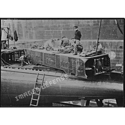 Ouvriers et marins à la maintenance de tubes lance-torpilles sur le sous-marin mouilleur de mines Saphir, en cale sèche dans un bassin de l'arsenal de Brest.
