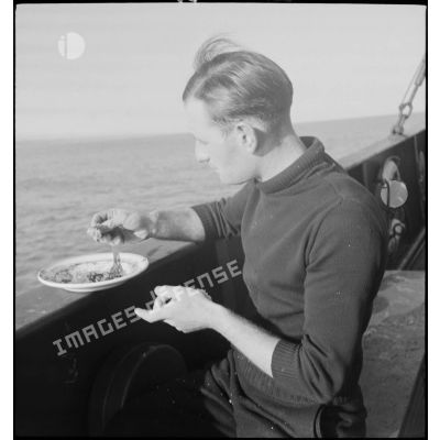 Un marin prend un repas sur le bastingage du pont d'un chalutier réquisitionné par la Marine nationale.