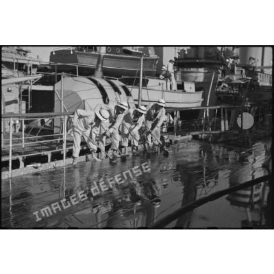 Des marins briquent le pont du croiseur lourd Duquesne.