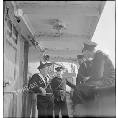 Des marins britanniques et français discutent sur le pont d'un navire marchand saisi par la Royal Navy et remis à la Marine nationale.